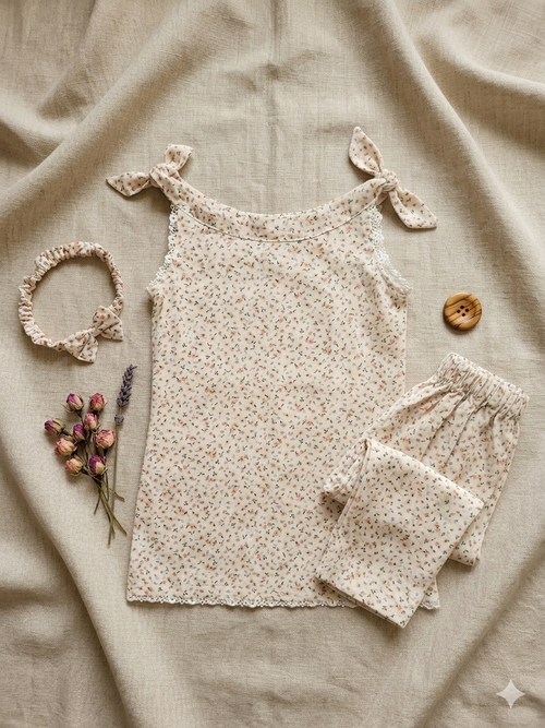 Baby girl floral outfit with shirt, trouser, and headband on a beige fabric background.